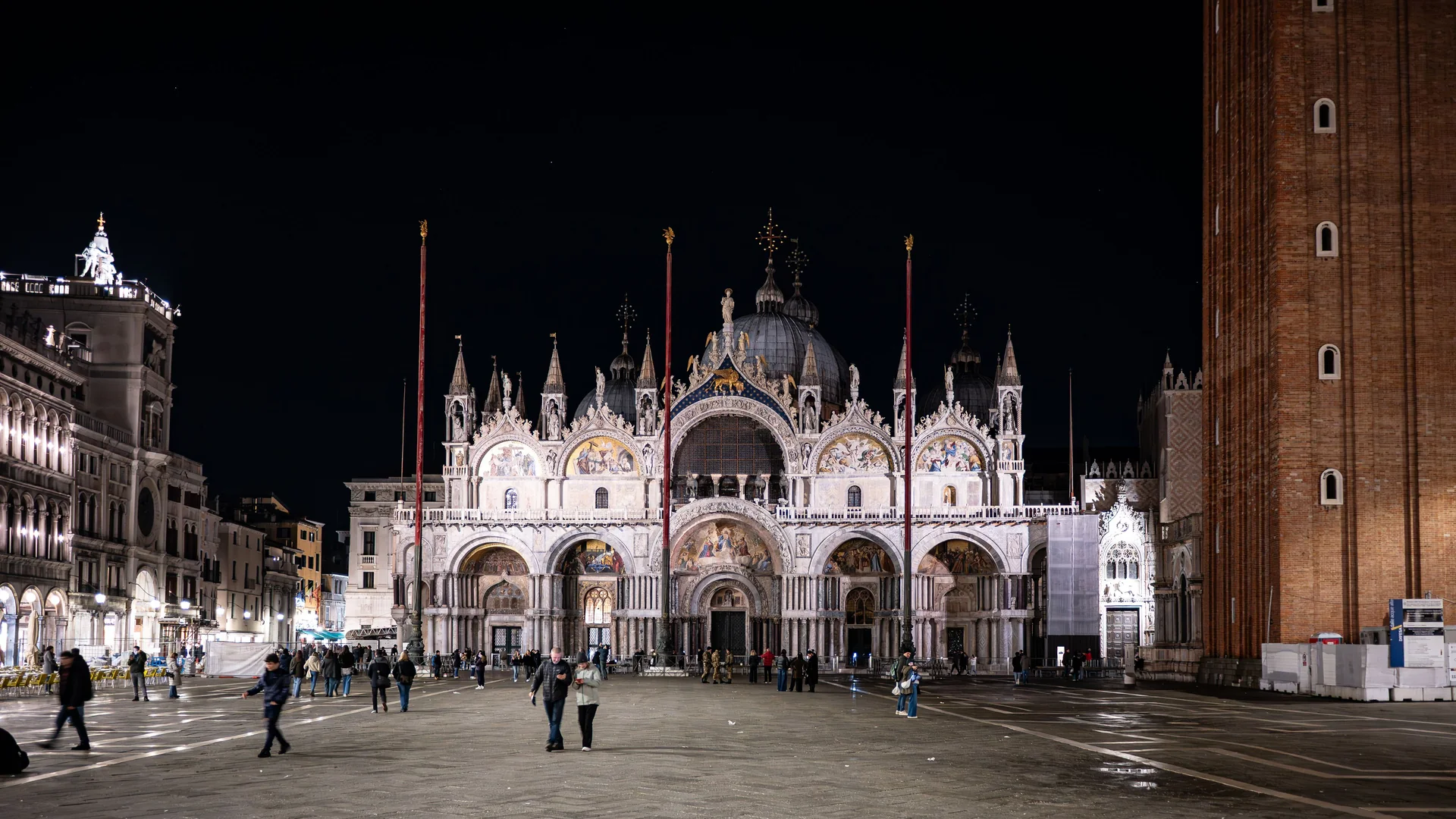 St Mark's Basilica illuminated at night, its mosaic facade lit gold above an almost empty Piazza San Marco
